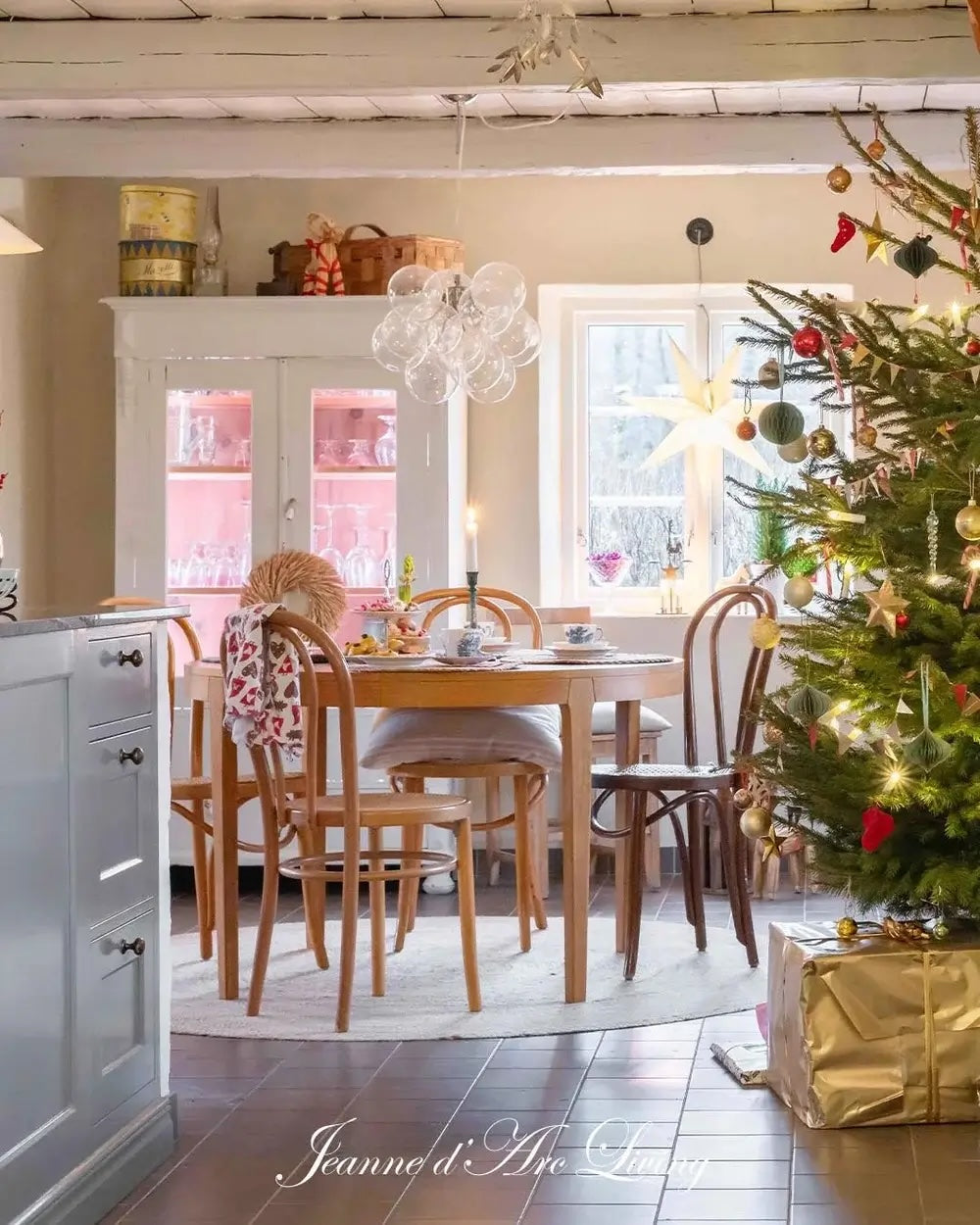 Dining room with a Christmas tree and decorated table, featuring a chandelier and gift-wrapped presents.