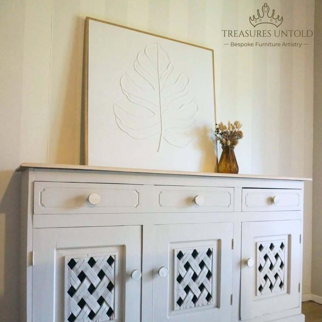 wooden sideboard cabinet painted with Blake & Taylor Furniture paint, colour Velvet taupe. styled room setting with a large leaf artwork leaning behind it and a small vase on top.