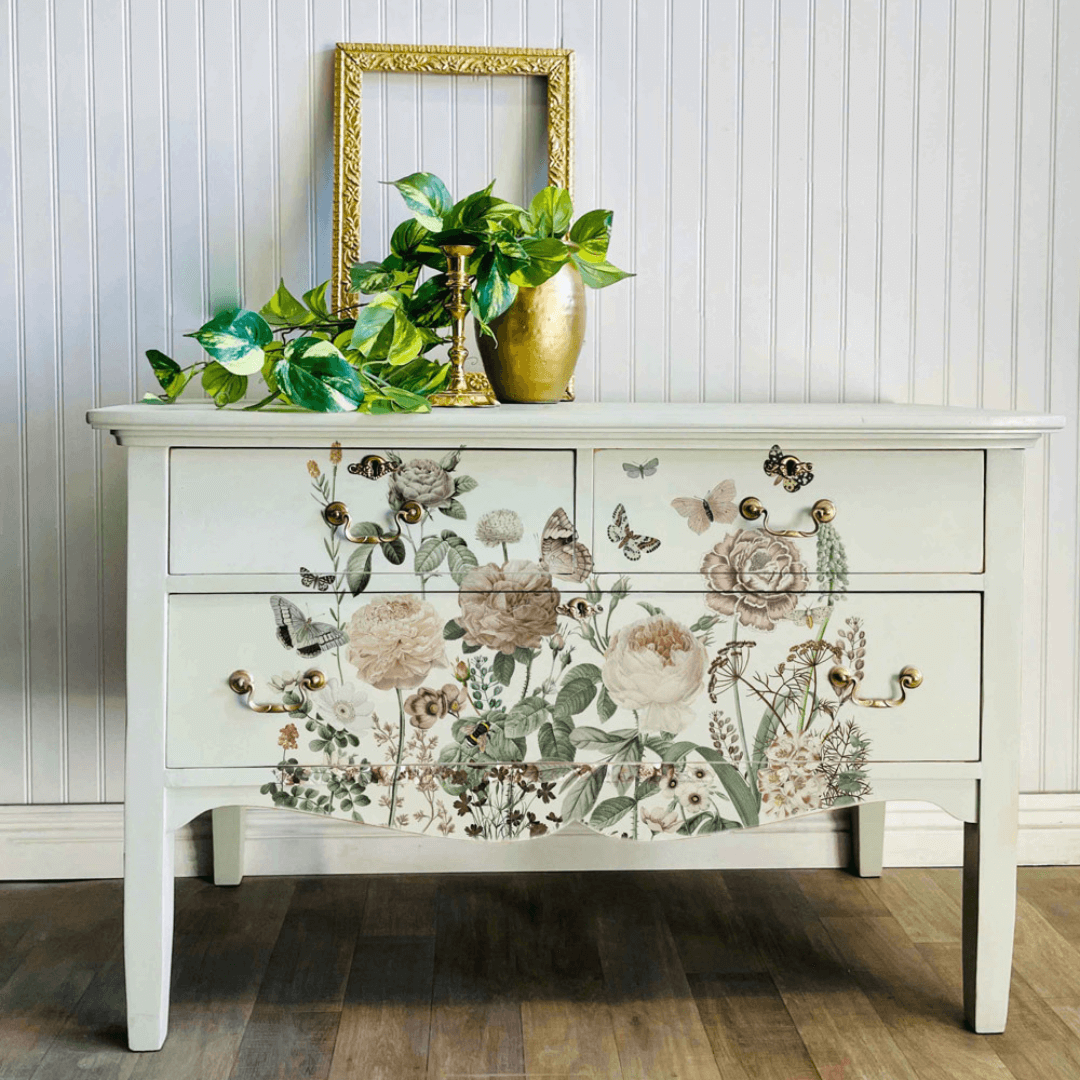 Decorative white dresser with floral decal against a light wooden paneled wall.