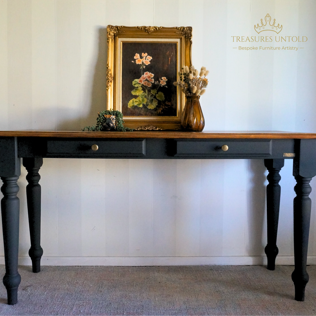 A console table with a natural wood top, painted with Blake & Taylor Furniture Paint, colour black, styled with a framed floral painting and a vase of dried flowers