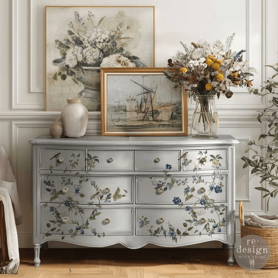 Decorative chest of drawers with floral patterns, framed artwork, and vases in a room setting.
