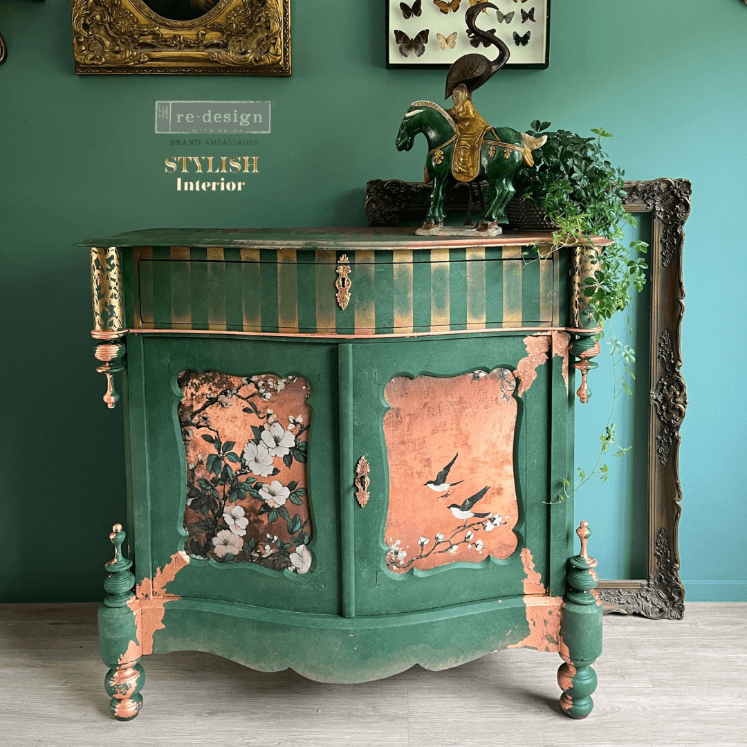 Decorative green cabinet with floral designs in a room with teal walls and framed pictures.