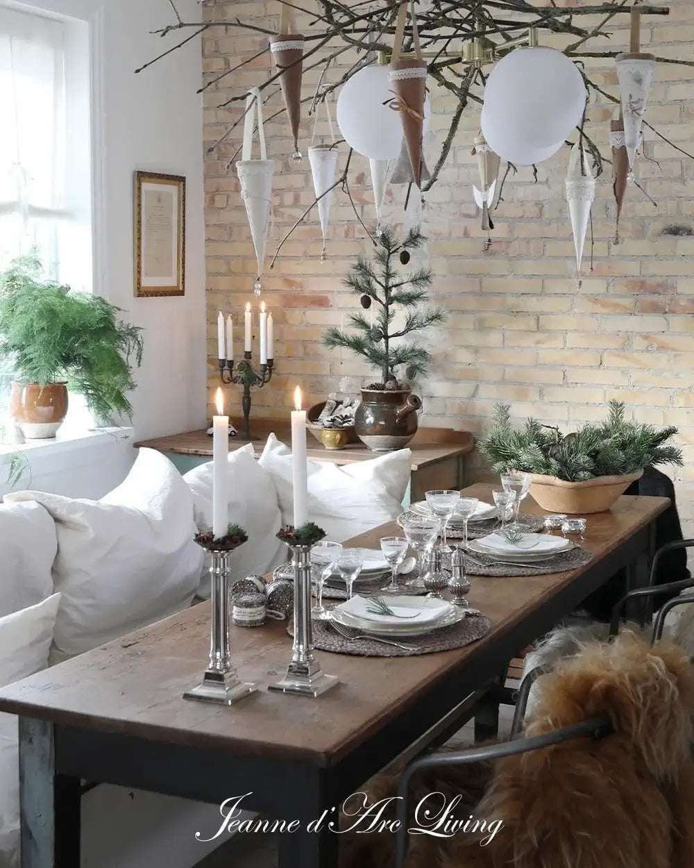 Dining room with a rustic table setting, candles, and decorative branches against a brick wall.