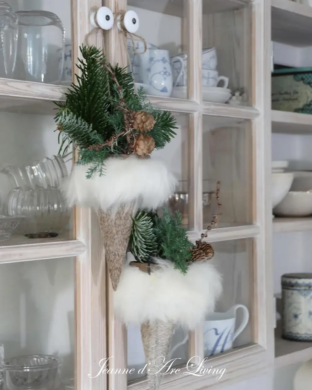 Decorative wreath with greenery and white feathers hanging on a glass cabinet.