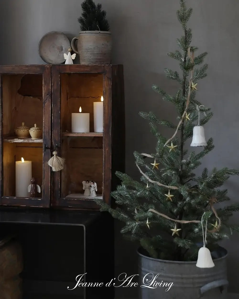 Decorative Christmas tree with star ornaments next to a wooden shelf with candles and small figurines.
