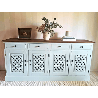 sideboard cabinet with a dark wood top, painted Blake & taylor Paint, colour Willow, featuring four lattice-patterned doors and three drawers. The cabinet is styled with a vase of greenery, a framed picture, and books on a woven rug against a striped wall.