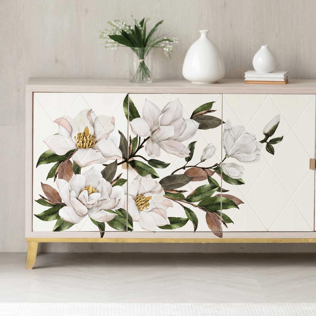 A modern sideboard cabinet with a white diamond-patterned front and large white magnolia floral decals on the doors, styled in a bright room with decorative vases on top.