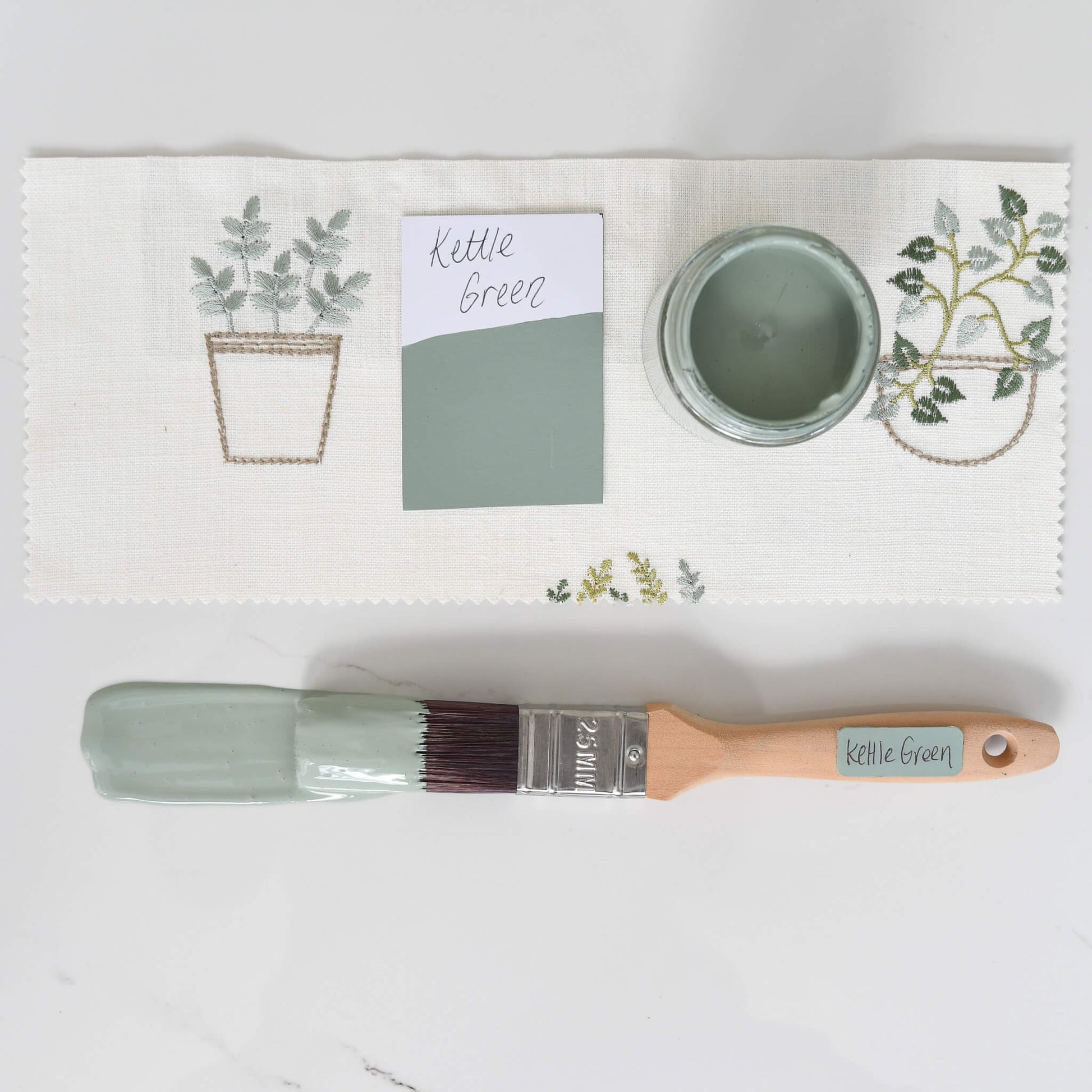 Fabric mood board with paintbrush dipped in 120ml pot of Blake & Taylor Kettle Green Chalk Furniture Paint